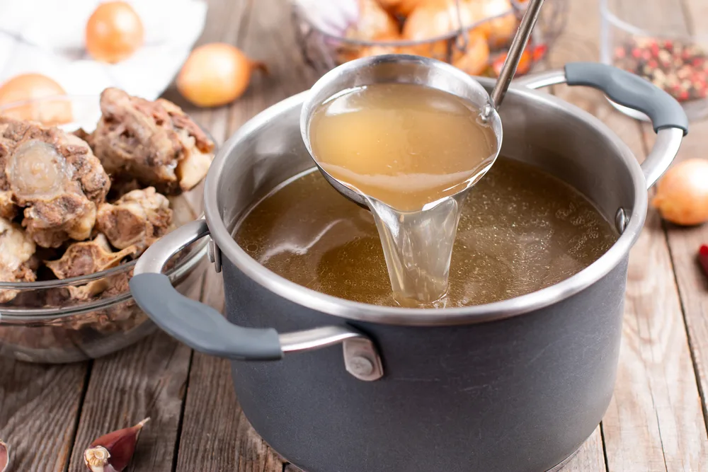 Bone broth being poured from ladle into pot.